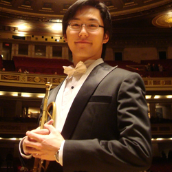 Apollo Lee in formal attire holding a trumpet on stage.