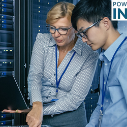 Two people working on a laptop in a server room, focused and engaged.