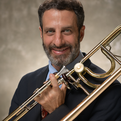Matthew Dixon smiling while holding a trombone against a dark background.
