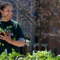 a student holding a plant while standing behind a table filled with other plants