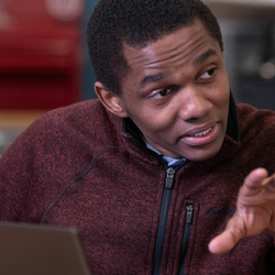 a student at his laptop explaining a concept to someone off-screen