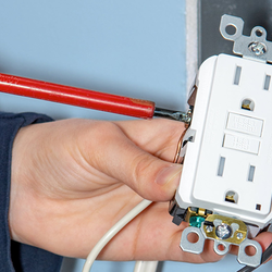 Hands installing an electrical outlet with a red screwdriver.