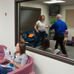 People sitting in a waiting room with red chairs and paintings on the wall.