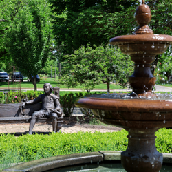 Fountain and bench with statues in a lush green park.