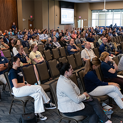 Audience seated in a large conference room, attentively watching a presentation.