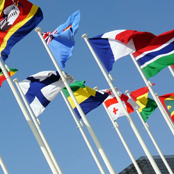 Flags of various countries waving against a clear blue sky.