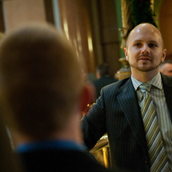 a man in a suit talking to others in a crowded business hall