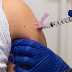 Vaccine injection into an arm by a person wearing blue gloves.