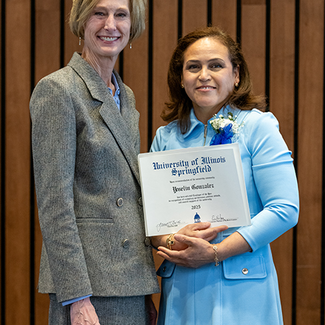 Two women smiling, one holding a certificate, standing indoors.