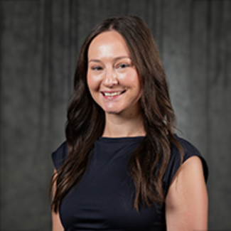 Smiling woman in a black dress against a dark background.