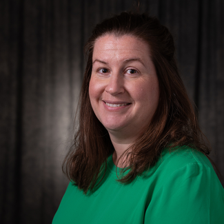 Smiling woman in a green top against a dark background.