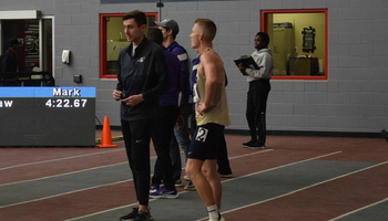 Emmons King in dark blue UIS windbreaker stands with UIS runners inside a track facility.