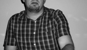 Man in plaid shirt playing keyboard in dim light, looking focused.