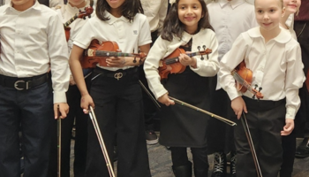 Children in white shirts holding violins and smiling.