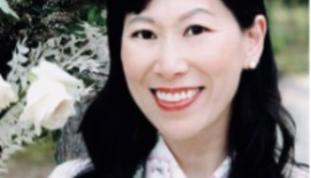 Smiling woman in floral dress near white roses outdoors.