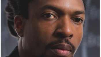 Dark-lit portrait of a serious-looking man with a black shirt.