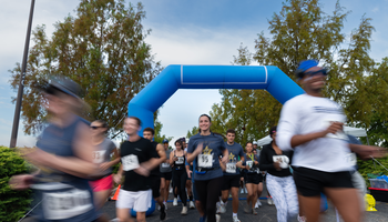 Runners starting a race under a blue inflatable arch, with trees and cloudy sky.