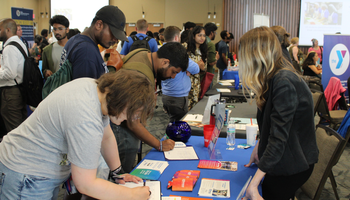 Busy career fair with people interacting at tables.