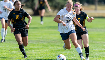 UIS soccer players in action on a green field, one leading with the ball.