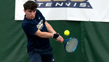 Pablo Herrera playing tennis indoors in blue UIS Uniform