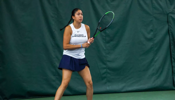 Cristina Mendoza Romero playing tennis indoors in white and blue UIS uniform