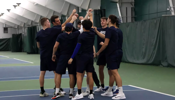 UIS men's tennis team in a huddle at indoor facility