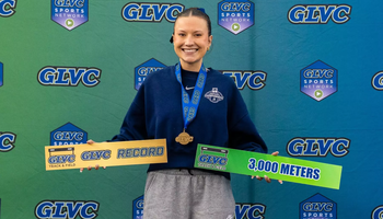 Madelyn Miller Ross poses in front of GLVC branded signage with All-GLVC medal and sign