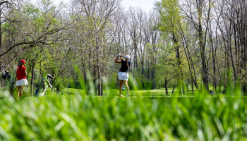 Elaine Grant golfing from afar, she is pictured in blue polo and white bottoms at GLVC Golf Tournament