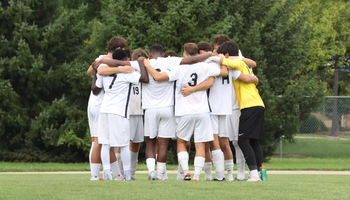 Men's Soccer Huddle on field pre-game, UIS players in white and yellow jerseys