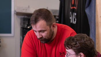Two men discussing something on a laptop, one pointing at the screen.