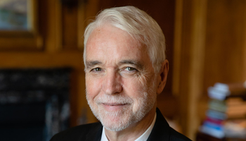 University of Illinois System President Tim Killeen in a suit smiling in a dimly lit room.