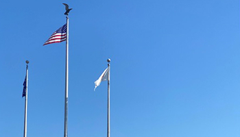 Three tall flagpoles with flags, clear blue sky, and a building in the background.