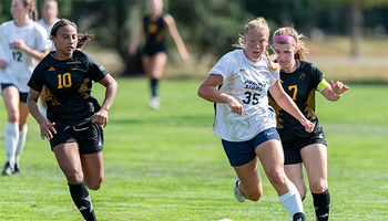 UIS soccer players in action on a green field, one leading with the ball.