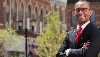 Professional person in a suit smiling, standing with arms crossed in a historic street.