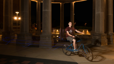 a male student riding his bike through the colonnade at night