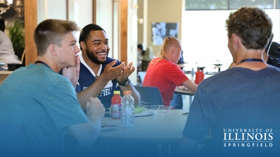 A group of people are sitting at a table, engaged in conversation at the University of Illinois Springfield.