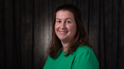 Smiling woman in a green top against a dark background.