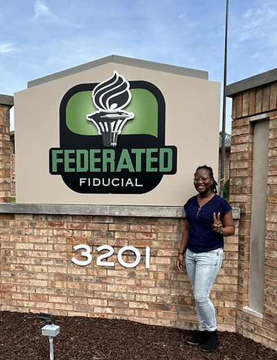 UIS student Wonder Odutola stands next to Federated Fiducial sign.