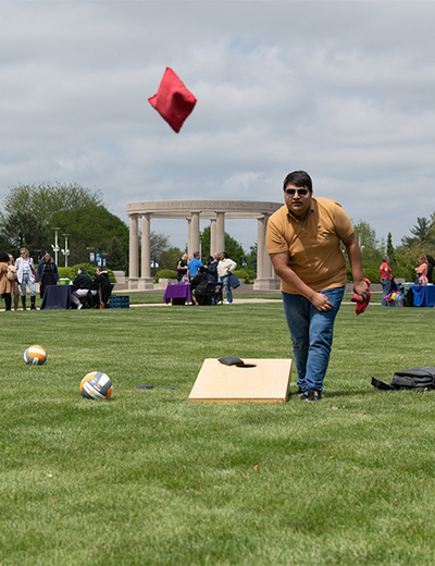 Students play lawn games during a campus health fair on the UIS quad, with booths and the colonnade visible in the background.