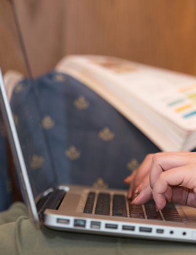 Close-up of a person typing on a laptop with an open textbook in the background.