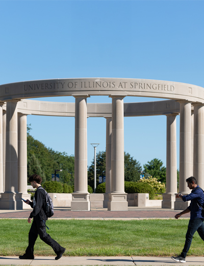 Two students walk in front of the UIS colonnade on a sunny day.