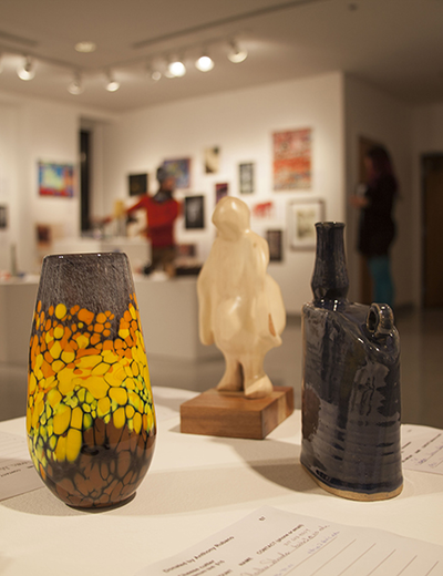 Art gallery with colorful vase, sculpture, and dark vase on display.