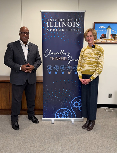 Two people standing beside a University of Illinois banner indoors.