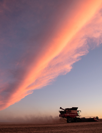 Combine harvester silhouetted against a vibrant sunset sky.