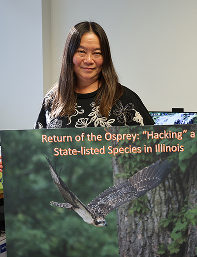 A woman standing, holding a large poster of an osprey in flight.