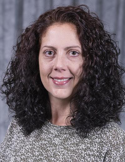 Smiling woman with curly hair against a gray backdrop.
