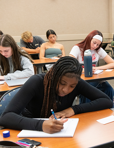 Students focused on writing at desks in a classroom.