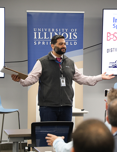 Man speaking at a presentation, University of Illinois Springfield banner behind him.