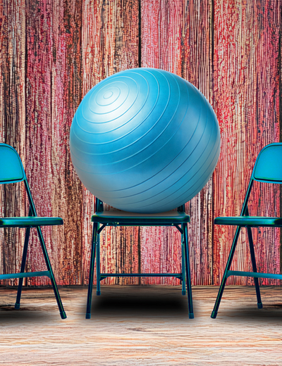 Blue exercise ball on chair between two folding chairs, wood-textured background.
