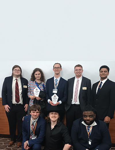 Eight people in formal attire, two holding awards, smiling indoors.